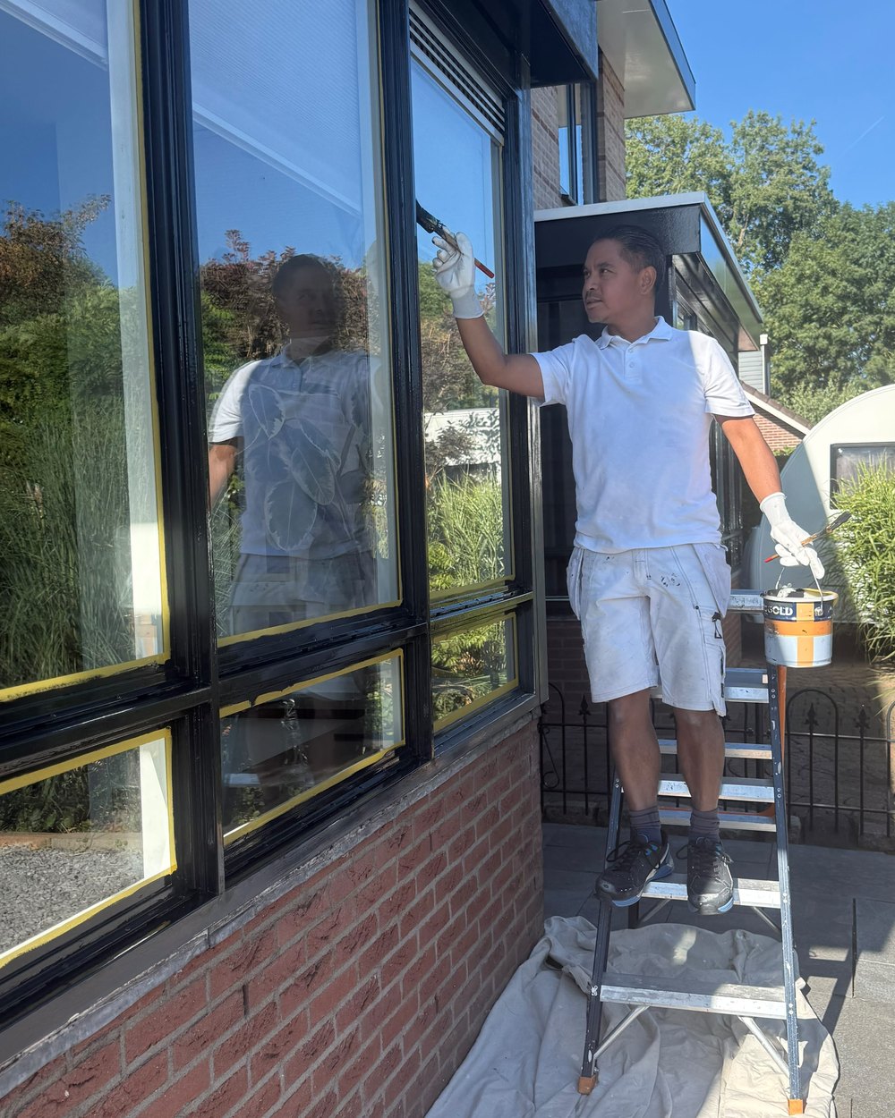 Arij Beekhuis op een trapje, bezig met het aflakken van een zwart kozijn